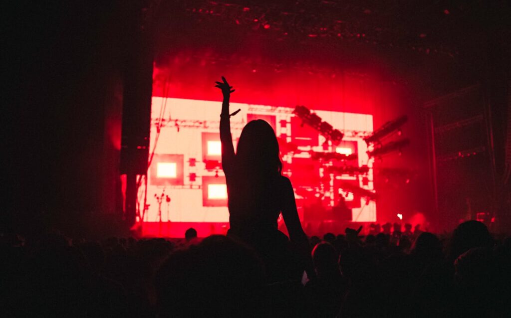 Silhouette of a woman raising her arm in a vibrant music festival with red lighting.