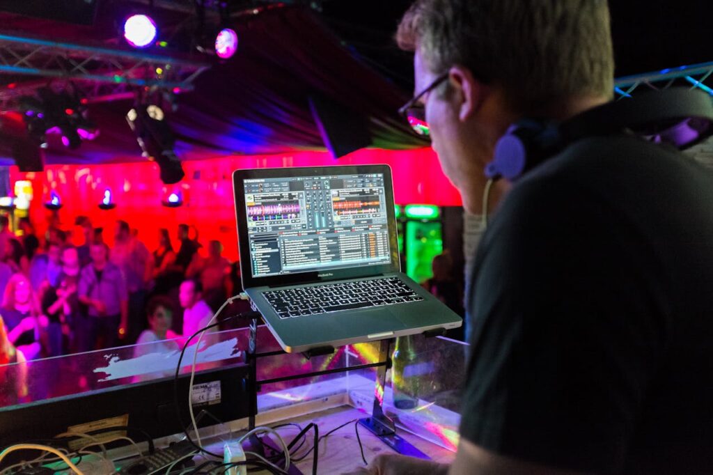 pexels-photo-358129 A DJ plays music using a laptop in a lively nightclub with a vibrant crowd and colorful lighting.