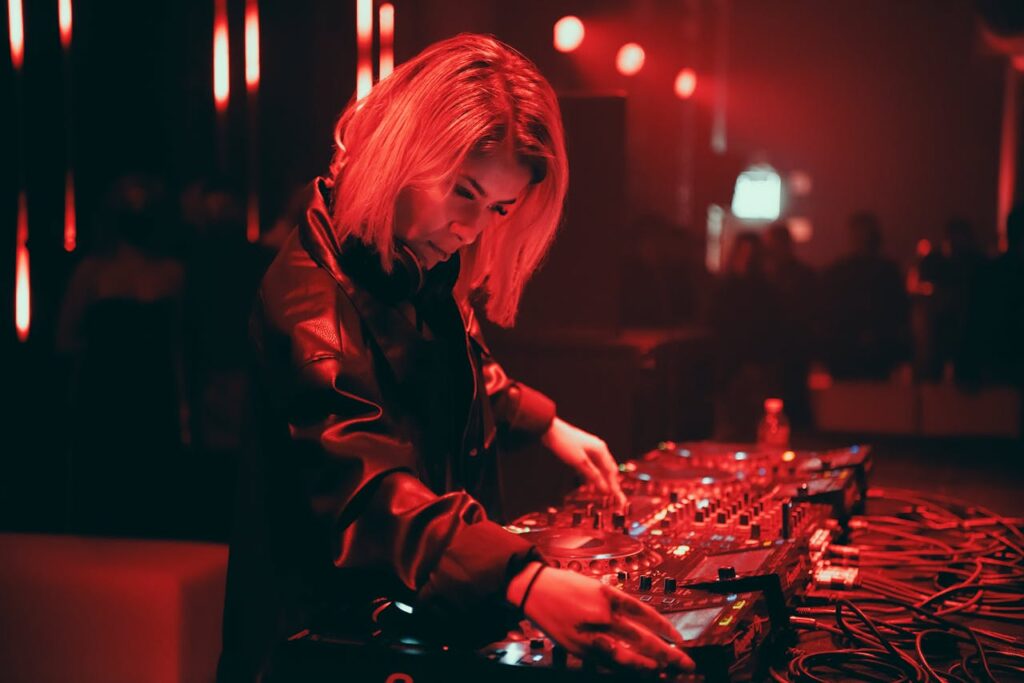 pexels-photo-8673526 A dynamic female DJ performs live at a bustling nightclub in red ambient lighting.